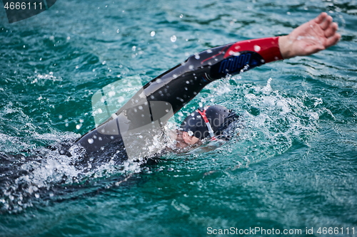 Image of triathlon athlete swimming on lake in sunrise wearing wetsuit