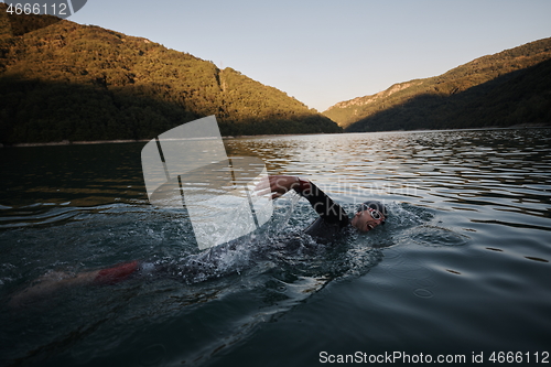 Image of triathlon athlete swimming on lake in sunrise wearing wetsuit