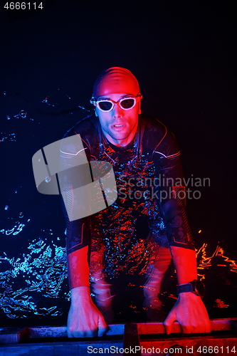 Image of authentic triathlete swimmer having a break during hard training on night neon gel light