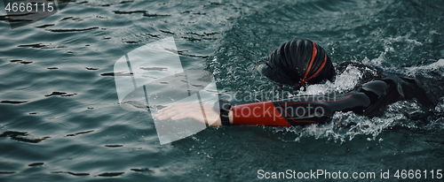 Image of triathlon athlete swimming on lake in sunrise wearing wetsuit