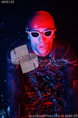 Image of authentic triathlete swimmer having a break during hard training on night neon gel light