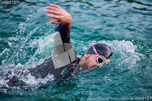 Image of triathlon athlete swimming on lake in sunrise wearing wetsuit