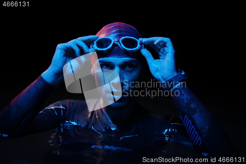 Image of authentic triathlete swimmer having a break during hard training on night neon gel light