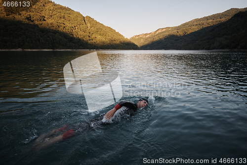 Image of triathlon athlete swimming on lake in sunrise wearing wetsuit