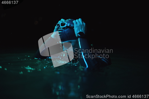 Image of authentic triathlete swimmer having a break during hard training on night neon gel light