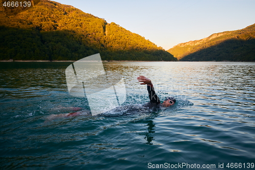 Image of triathlon athlete swimming on lake in sunrise wearing wetsuit