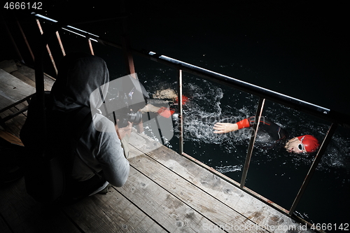 Image of videographer taking action shot of triathlon swimming athlete at night