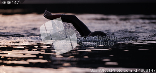 Image of triathlon athlete swimming on lake in sunrise wearing wetsuit