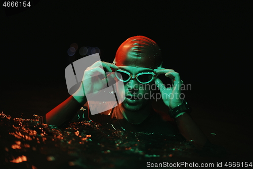 Image of authentic triathlete swimmer having a break during hard training on night neon gel light