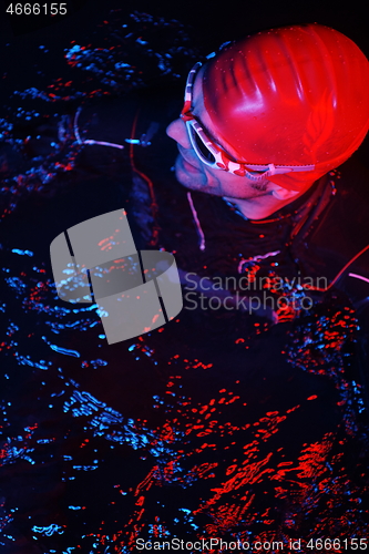 Image of authentic triathlete swimmer having a break during hard training on night neon gel light