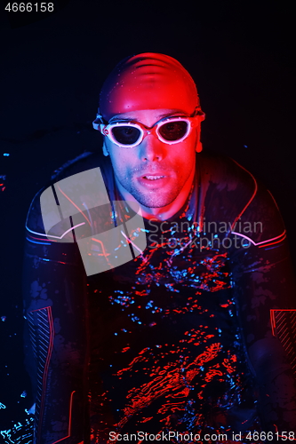 Image of authentic triathlete swimmer having a break during hard training on night neon gel light