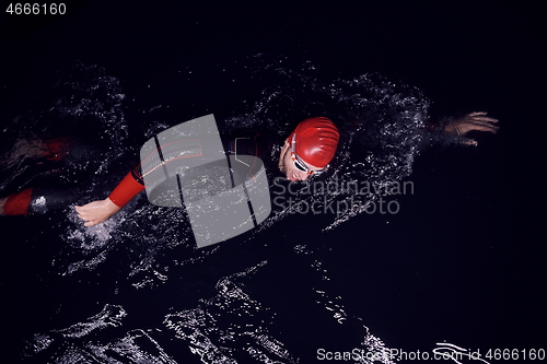 Image of triathlon athlete swimming in dark night wearing wetsuit