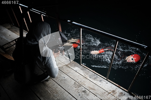 Image of videographer taking action shot of triathlon swimming athlete at night