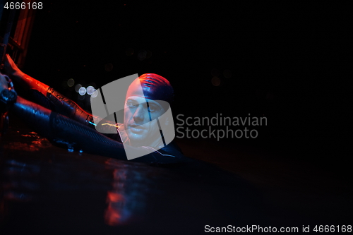 Image of authentic triathlete swimmer having a break during hard training on night neon gel light