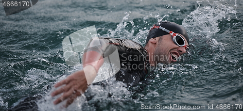 Image of triathlon athlete swimming on lake in sunrise wearing wetsuit