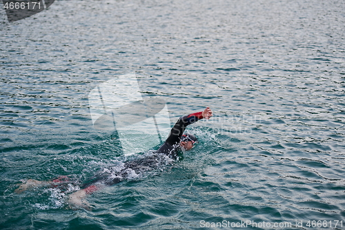 Image of triathlon athlete swimming on lake in sunrise wearing wetsuit