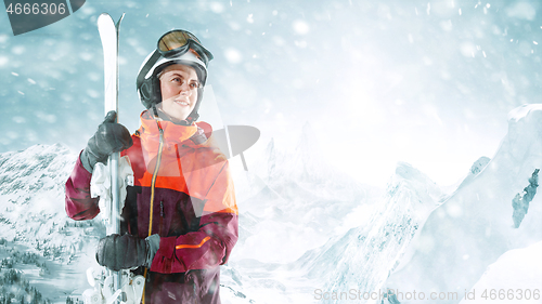 Image of Female skier standing with skies in one hand on background mountain landscape