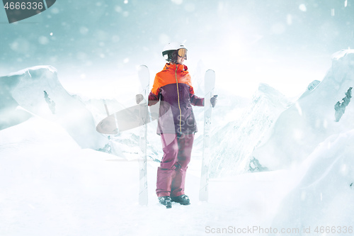 Image of Female skier standing with skies in one hand on background mountain landscape