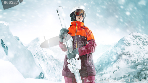 Image of Female skier standing with skies in one hand on background mountain landscape