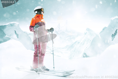 Image of Female skier standing with skies in one hand on background mountain landscape