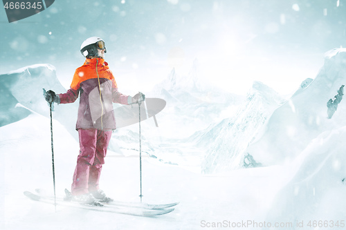 Image of Female skier standing with skies in one hand on background mountain landscape