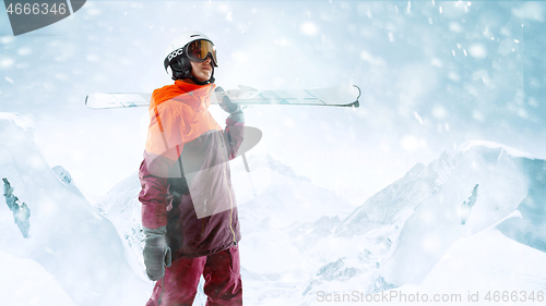 Image of Female skier standing with skies in one hand on background mountain landscape