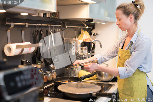 Image of Stay at home housewife woman cooking in kitchen, stir frying dish in a saucepan, preparing food for family dinner.