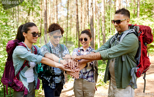 Image of friends with backpacks stacking hands in forest