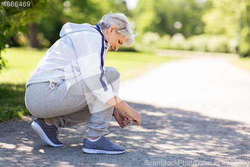 Image of senior woman tying sport shoe laces at summer park