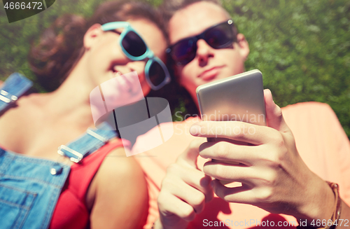 Image of teenage couple with smartphone lying on grass