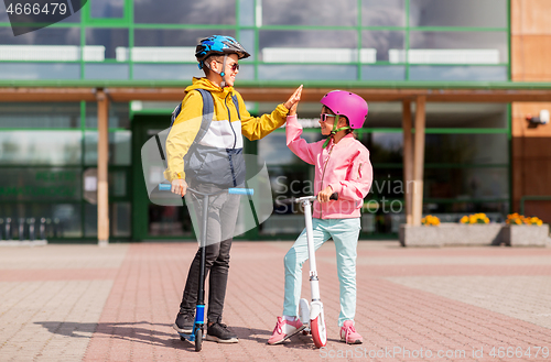 Image of school kids riding scooters and making high five