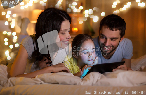 Image of family with tablet pc in bed at night at home