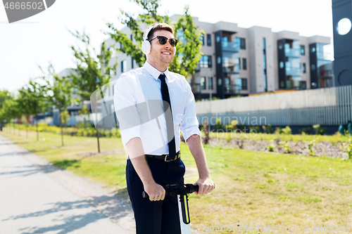 Image of businessman with headphones riding scooter in city