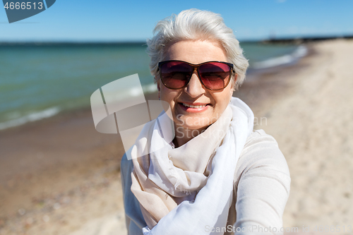 Image of senior woman in sunglasses taking selfie on beach