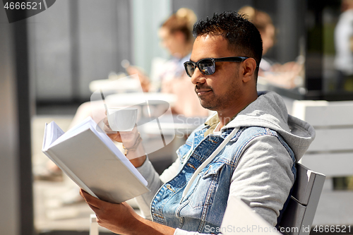Image of man reading book and drinking coffee at city cafe