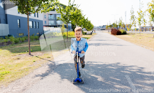 Image of happy little boy riding scooter in city