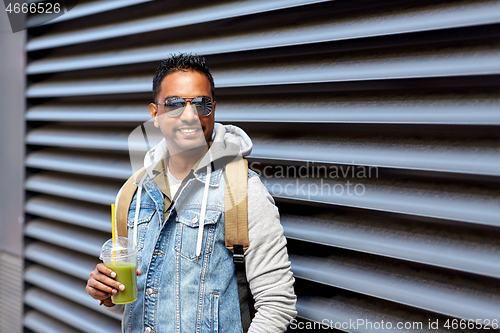 Image of man with backpack drinking smoothie on street