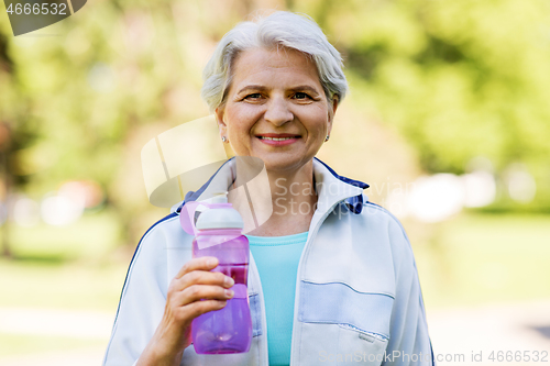 Image of sporty senior woman with bottle of water at park