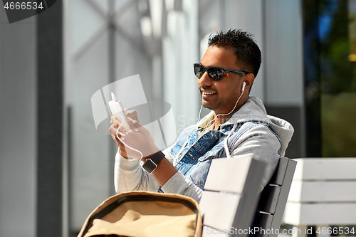 Image of man with earphones and smartphone on city street