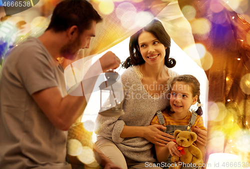 Image of happy family playing in kids tent at night at home