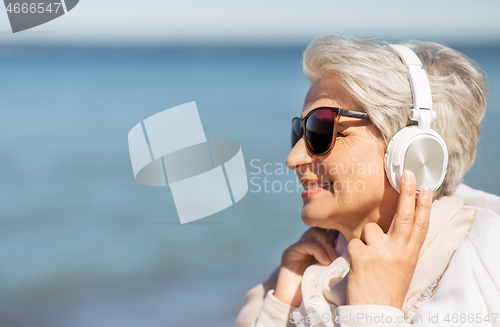 Image of old woman in headphones listens to music on beach
