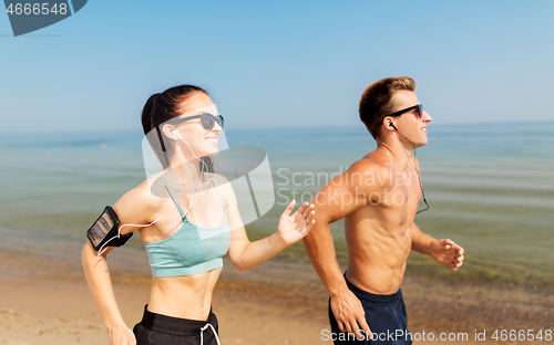 Image of couple with phones and arm bands running on beach