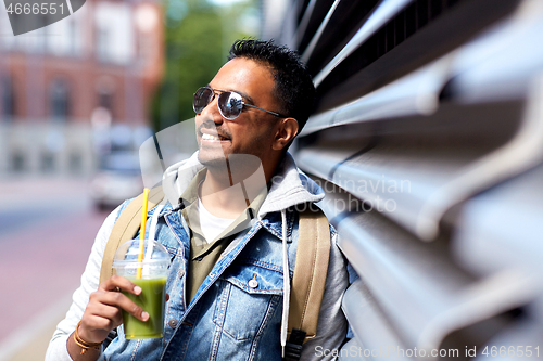 Image of man with backpack drinking smoothie on street