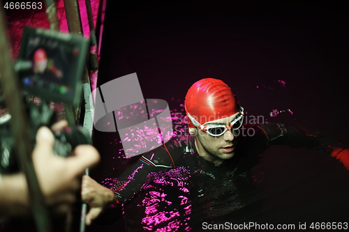 Image of videographer taking action shot of triathlon swimming athlete at night