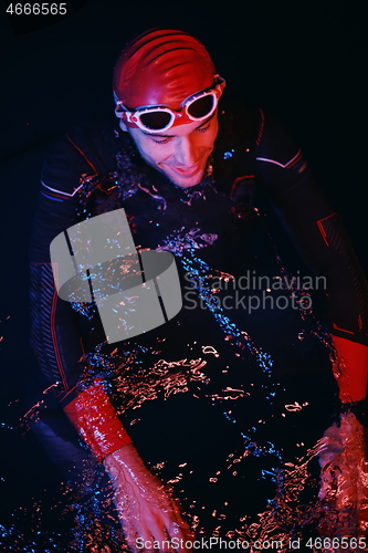 Image of authentic triathlete swimmer having a break during hard training on night neon gel light