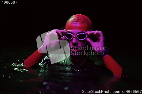 Image of authentic triathlete swimmer having a break during hard training on night neon gel light