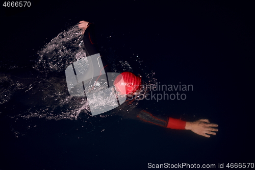 Image of triathlon athlete swimming in dark night wearing wetsuit