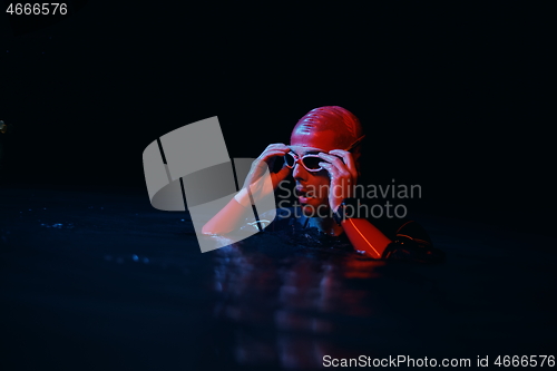 Image of authentic triathlete swimmer having a break during hard training on night neon gel light