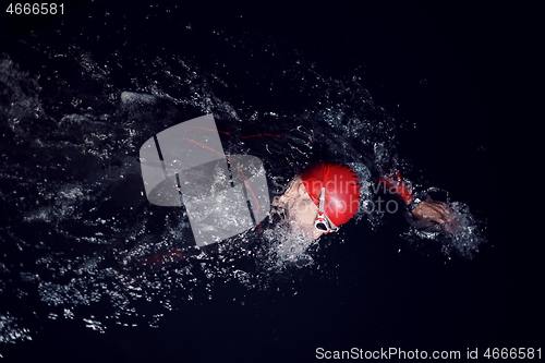 Image of triathlon athlete swimming in dark night wearing wetsuit