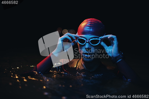 Image of authentic triathlete swimmer having a break during hard training on night neon gel light